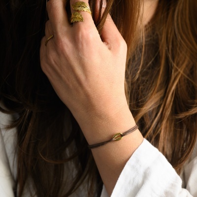 Pulseira fina com pendente em forma de concha em cordão castanho no braço esquerdo