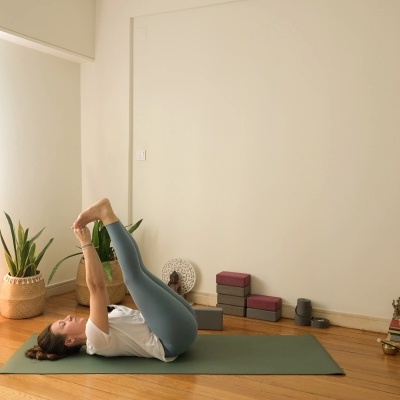 Tapete de yoga verde numa sala com piso de madeira, planta, blocos de yoga e objetos decorativos