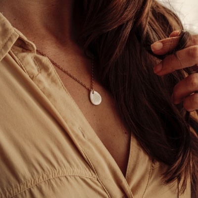 Colar com pendente de concha em corrente dourada usado por pessoa com camisa bege