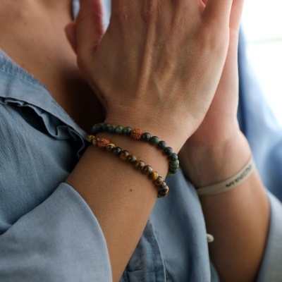 Braceletes de contas verdes e castanhas no pulso de pessoa com camisa azul clara