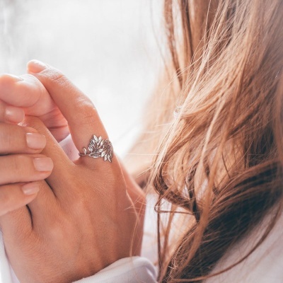 Anel prateado com design de folhas num dedo de mão clara