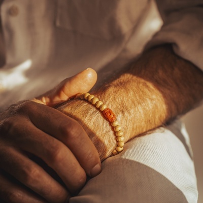 Pulseira de contas de madeira clara e laranja no pulso de uma pessoa com camisa branca