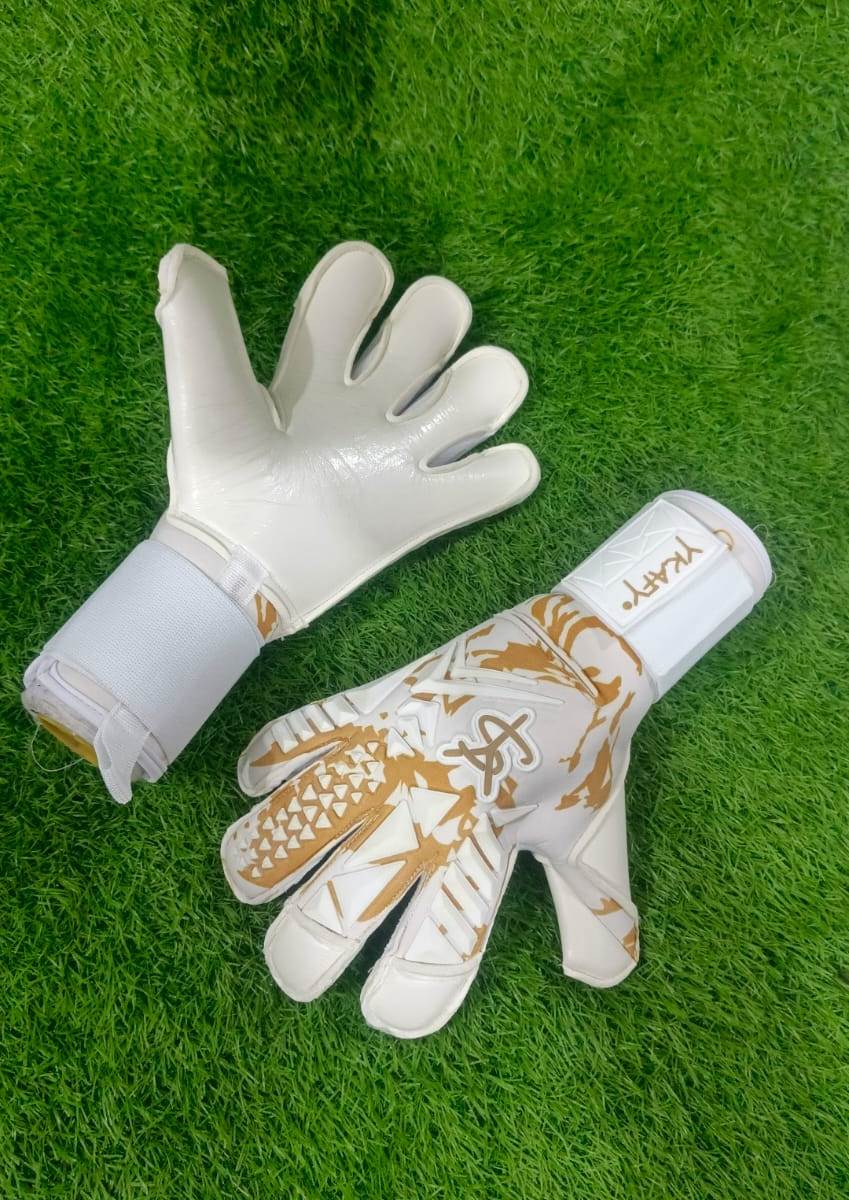 Luvas de guarda-redes de futebol branco com detalhes dourados sobre relva sintética verde.