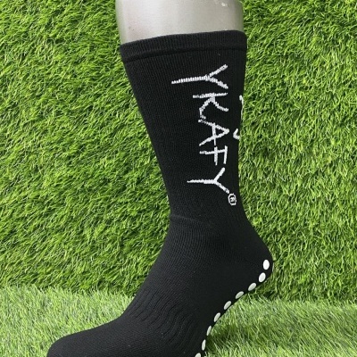 Meia preta desportiva com texto branco e sola antiderrapante sobre relva artificial