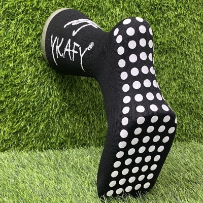 Meia preta com pontos antiderrapantes brancos e texto YKAFY sobre relva