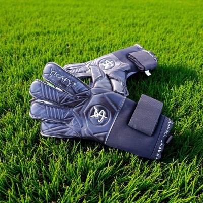 Luvas de guarda-redes pretas com detalhes e inscrições sobre relva verde