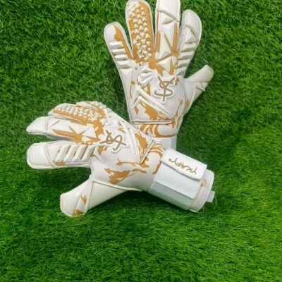Luvas de guarda-redes de futebol brancas e castanhas sobre relva artificial.
