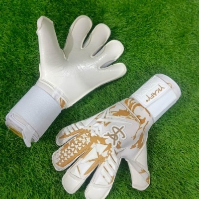 Luvas de guarda-redes de futebol branco com detalhes dourados sobre relva sintética verde.
