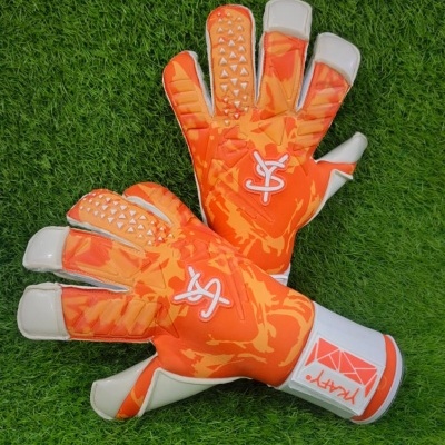 Luvas de guarda-redes laranja e branco sobre relva artificial.