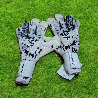 Luvas de guarda-redes de futebol brancas com detalhes pretos sobre relvado verde.