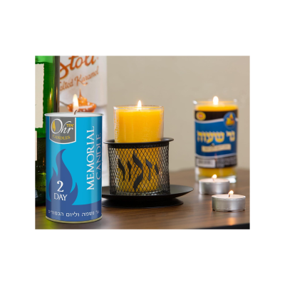 Vela memorial amarela com base metálica preta e velas em embalagens azuis com texto em inglês e hebraico numa mesa de madeira