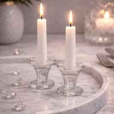 Dois castiçais transparentes com velas acesas sobre bandeja de mármore cinza.