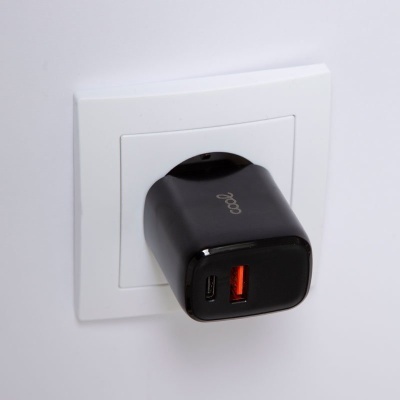 Carregador de parede preto com portas USB ligado a tomada branca