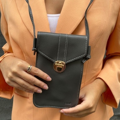 Mala pequena preta com fecho dourado e alça fina segurada por pessoa com casaco laranja