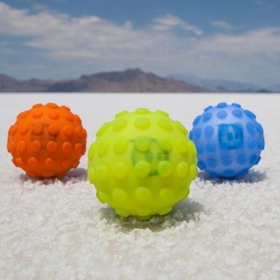 Três bolas coloridas texturizadas sobre superfície branca com montanhas ao fundo