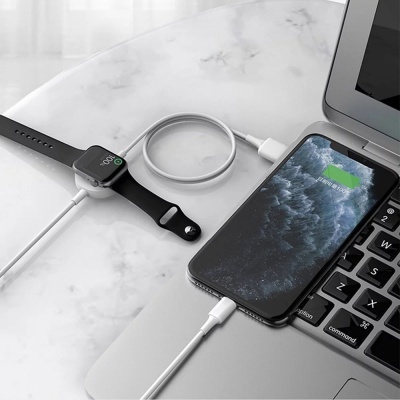 Relógio inteligente e smartphone a carregar sobre mesa branca ao lado de portátil