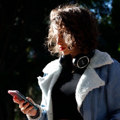 Mulher com casaco com pêlo e auscultadores a usar smartphone ao ar livre