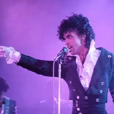 Cantor a cantar num microfone vestido com fato preto e camisa branca