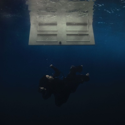 Pessoa com roupa de mergulho azul escuro sob a água perto de uma estrutura branca