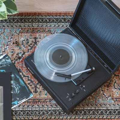 Gira-discos preto com disco vinil transparente num tapete com padrão oriental