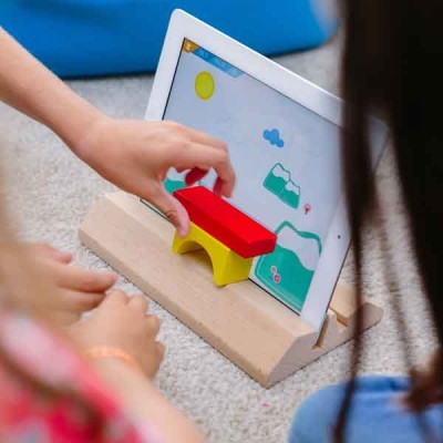 Tablet branco numa base de madeira com crianças a jogar com peças de madeira coloridas