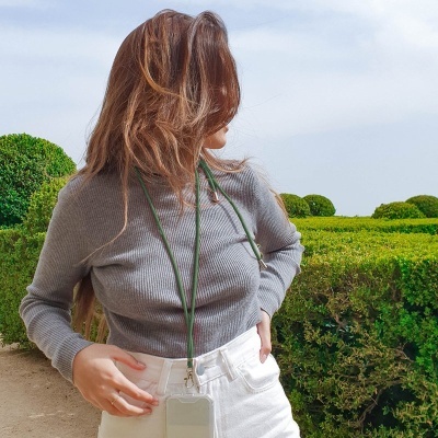 Mulher com camisola cinzenta e suporte para telemóvel verde num jardim