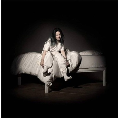 Pessoa sentada numa cama branca com roupa de cama branca num ambiente escuro