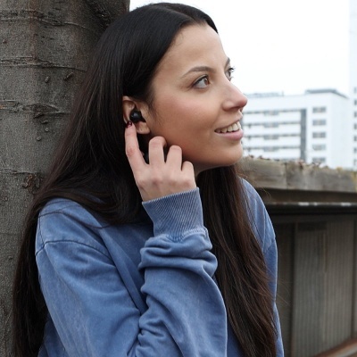 Mulher com auriculares sem fios pretos num ambiente urbano junto a uma árvore