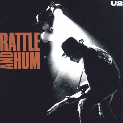 Capa de álbum musical com duas figuras masculinas em silhueta sob luz forte, texto 'BATTLE AND HUM' e 'U2'.