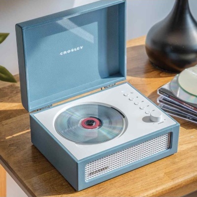 Toca-discos portátil Crosley azul claro e branco aberto numa mesa de madeira