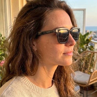 Óculos de sol pretos com lentes espelhadas usados por mulher com camisola bege na varanda