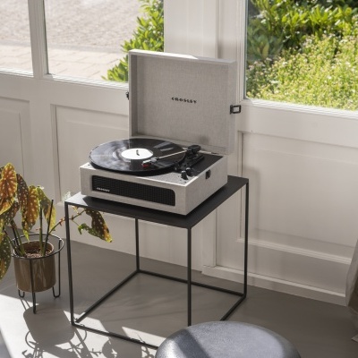 Tocadiscos Crosley branco com tampa aberta em mesa preta num ambiente iluminado.