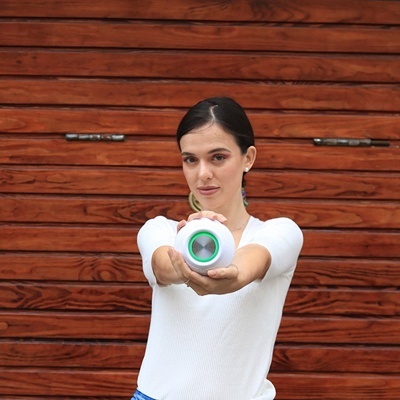 Mulher com blusa branca segurando dispositivo circular branco com realce verde em porta de madeira