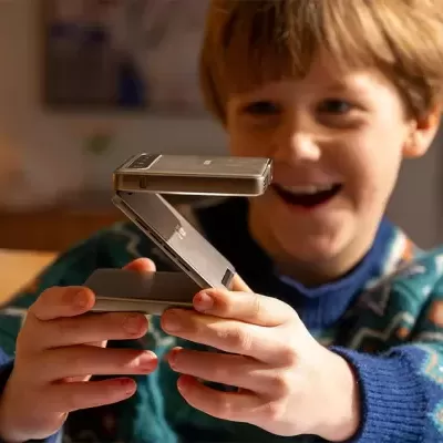 Criança feliz a segurar um telefone dobrável cinza metálico no interior