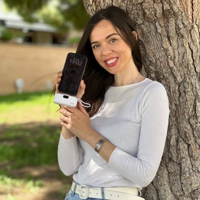 Mulher com smartphone e carregador portátil branco junto a árvore