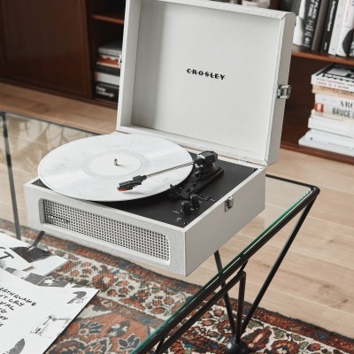 Gira-discos branco CROSLEY em mesa de vidro numa sala com estante e livros