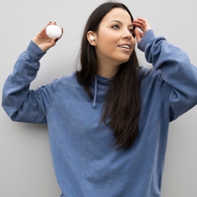 Mulher com hoodie azul e auriculares brancos, segurando estojo oval branco