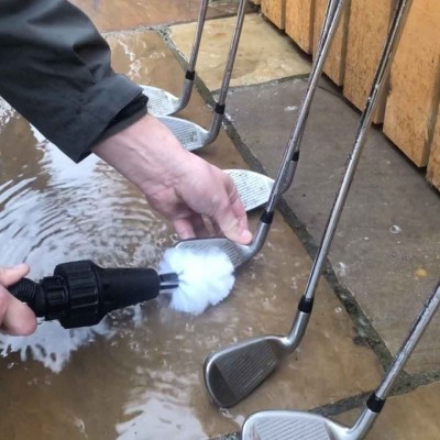 Pessoa a limpar tacos de golfe com escova branca e dispositivo preto em chão molhado