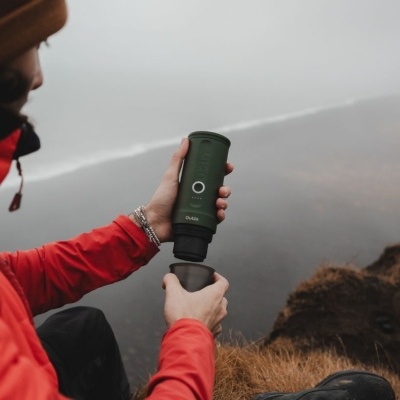 Termo portátil verde fosco com tampa preta usado ao ar livre próximo ao mar