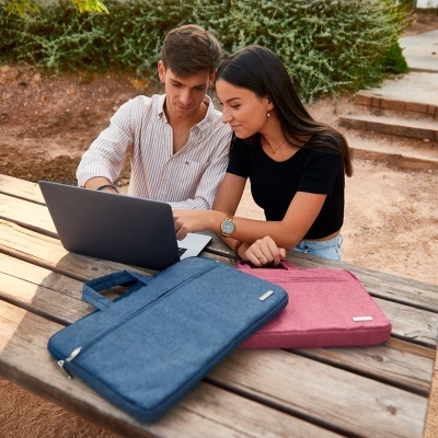 Dois jovens sentados num banco de madeira ao ar livre com portátil e duas capas para portátil azul e rosa