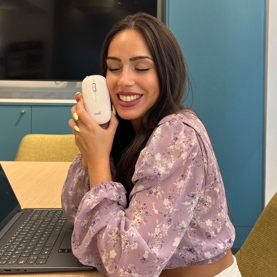 Mulher com blusa lilás e rato de computador branco ao lado de portátil preto