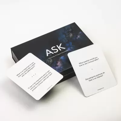 Caixa preta com padrão abstrato azul e roxo com o texto 'ASK' e duas cartas brancas com texto em inglês e português sobre fundo branco
