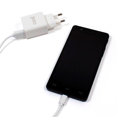 Smartphone preto a ser carregado com cabo e adaptador branco com texto 'cool'