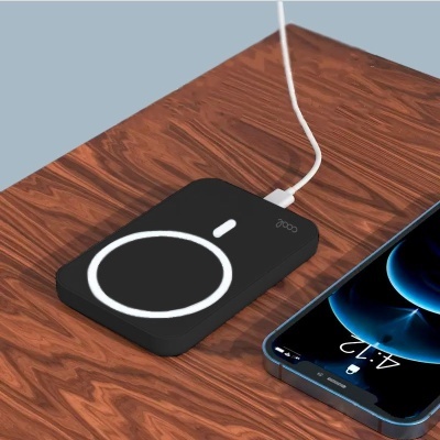 Carregador portátil preto com cabo ligado a smartphone azul escuro sobre mesa de madeira