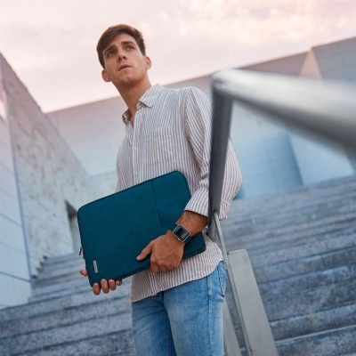 Homem jovem com camisa de riscas, jeans e pasta azul em escadas urbanas