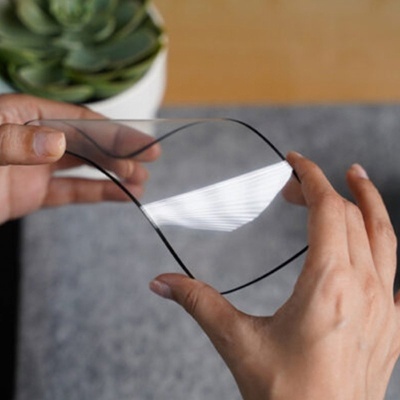 Lente ocular retangular arredondada com armação preta segurada por mãos sobre mesa cinzenta