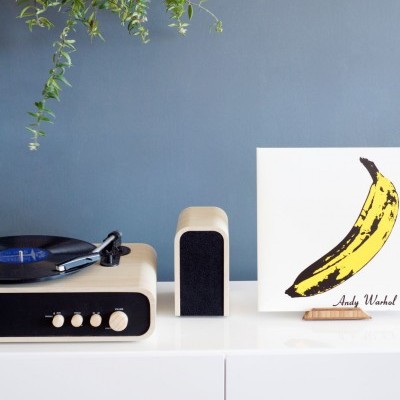 Gira-discos de madeira, altifalante, arte de banana Andy Warhol, móvel branco, parede azul, planta pendente