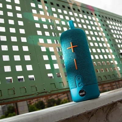 Coluna de som portátil azul com botões laranja encostada em superfície branca