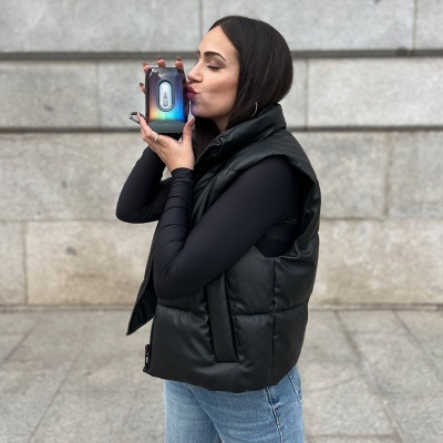 Mulher segurando caixa eletrônica preta com visor digital e detalhes coloridos