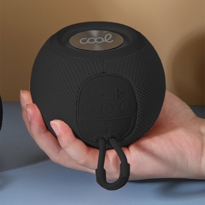 Coluna portátil preta com textura malha, botões de controlo e gancho, com a palavra 'cool' no topo